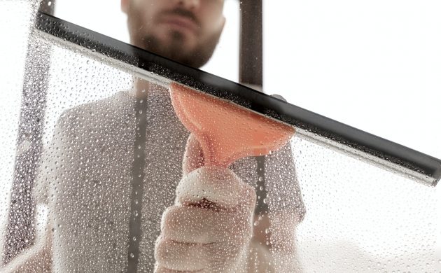 A male washes windows at home. Cleaning a windows with a squeegee, close up.