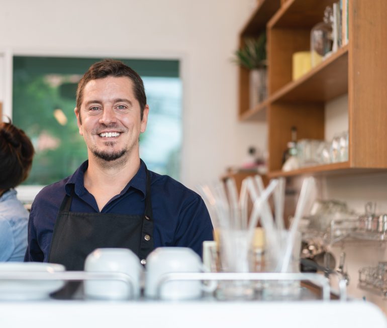 Male barista owners in apron smiling and service to client in coffee shop